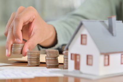 hands holding coins on a table with a small house